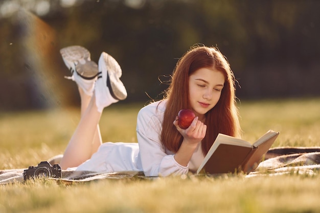 Con il libro e una mela La giovane ragazza è sul campo durante il giorno soleggiato con un bel fine settimana