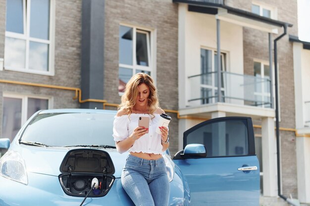 Con il telefono Giovane donna in abiti casual con il suo elettromobile all'aperto durante il giorno