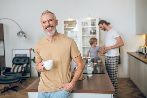 Con la famiglia. Uomo dai capelli grigi che mangia il caffè del mattino e si sente bene