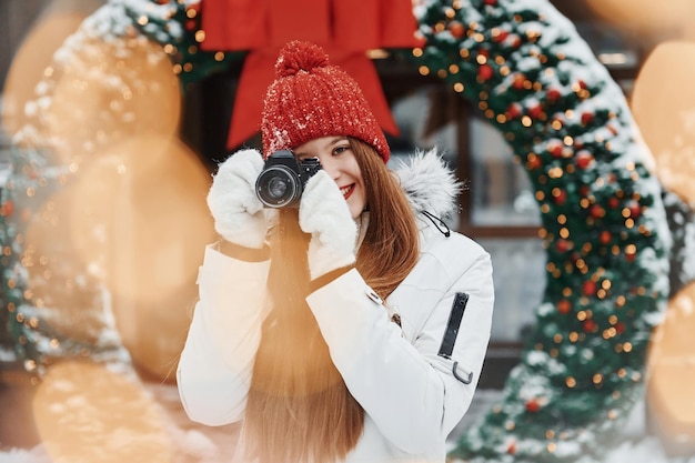 Con la fotocamera in mano Felice giovane donna in piedi all'aperto e celebrare le vacanze di Natale