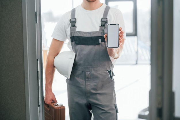Con lo smartphone in mano Il riparatore è in piedi all'interno della stanza moderna