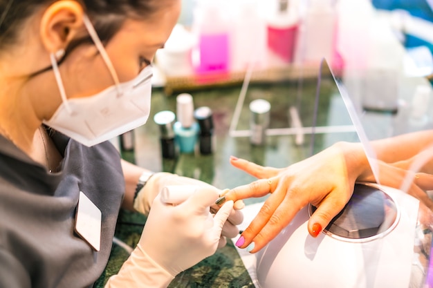 Con maschera per il viso che dipinge le unghie colorate del cliente. Riapertura dopo la pandemia di corod-19. Salone per manicure e pedicure. Coronavirus