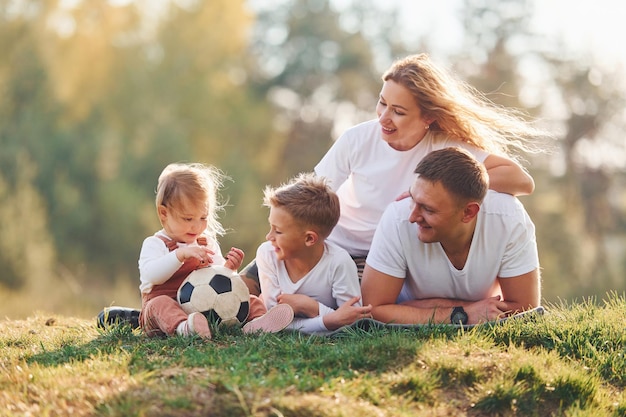 Con pallone da calcio Famiglia felice sdraiato all'aperto vicino alla foresta Con figlia e figlio