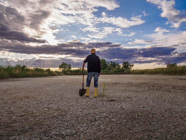 Con stivali di gomma per il campo asciutto L'agricoltore va con i suoi stivali di gomma e la sua pala in un campo arido Vista da dietro Concetto di siccità