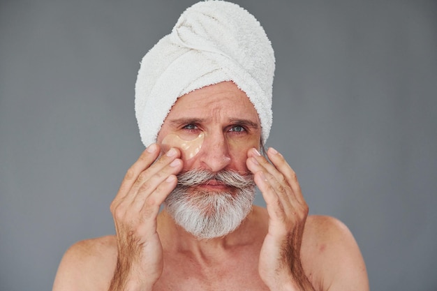 Con un asciugamano bianco sulla testa L'uomo anziano moderno ed elegante con capelli grigi e barba è al chiuso