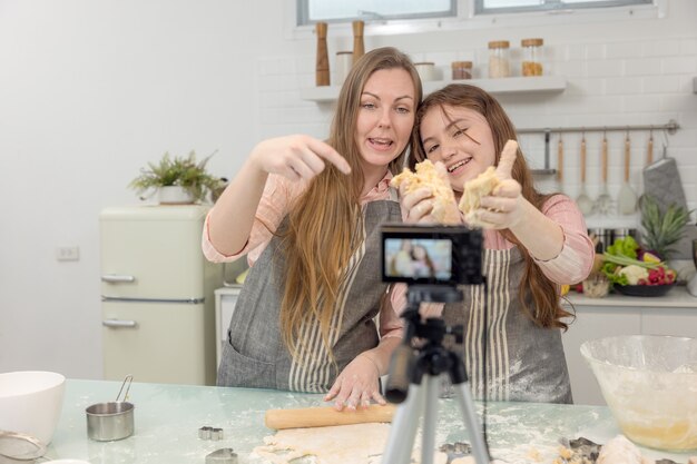 Con una fotocamera digitale dal vivo in cucina, madre e figlia sorridono e si divertono mentre preparano l'impasto per biscotti insieme, la figlia impara a fare i biscotti con sua madre.