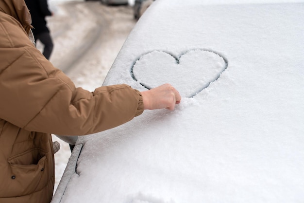 Con una mano in una giacca disegna un cuore sul parabrezza in inverno nella neve