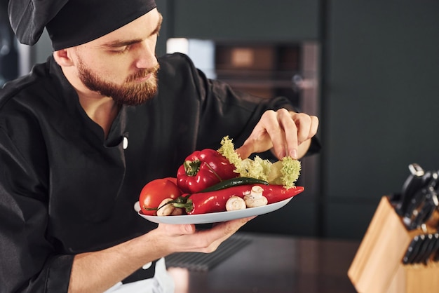 Con verdure Giovane chef professionista in uniforme che lavora in cucina