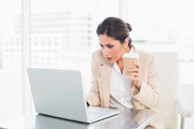 Concentrando il caffè bevente della donna di affari mentre lavorando al computer portatile