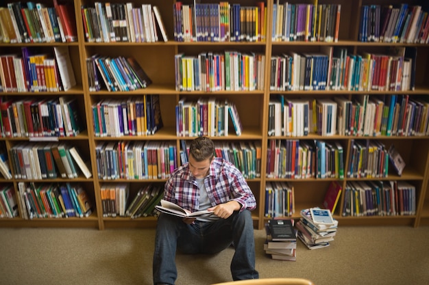 Concentrando il giovane studente che si siede sulla lettura del pavimento delle biblioteche