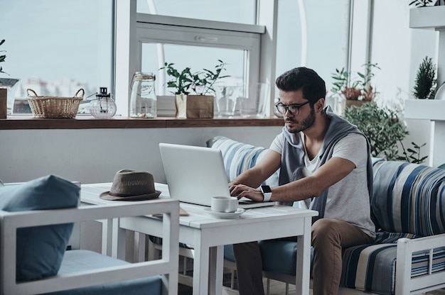 Concentrandosi sul progetto. Bel giovane uomo moderno in occhiali usando il computer