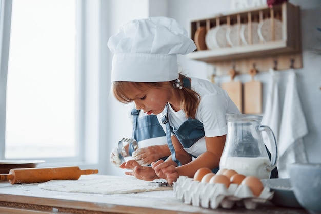 Concentrarsi in cottura. Bambini di famiglia in uniforme bianca da chef che preparano il cibo in cucina.