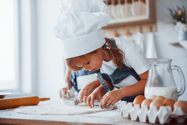 Concentrarsi in cottura. Bambini di famiglia in uniforme bianca da chef che preparano il cibo in cucina.