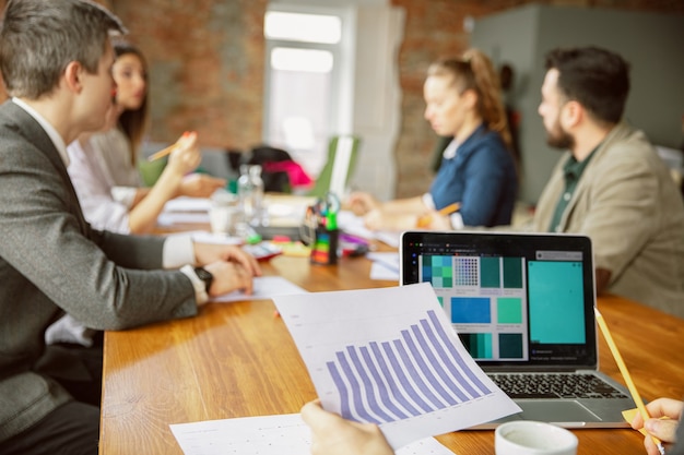 Concentrarsi sul computer portatile. Gruppo di giovani professionisti che hanno una riunione. Diversi gruppi di colleghi discutono di nuove decisioni, piani, risultati, strategia. Creatività, posto di lavoro, affari, finanza, lavoro di squadra.