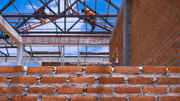 Concentrarsi sul muro di mattoni con sfocatura dello sfondo dei lavoratori che lavorano sulla struttura del tetto in cantiere