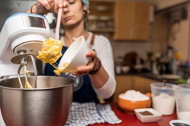 Concentrarsi sulle mani della cuoca che mettono il burro nella ciotola del miscelatore elettrico per la preparazione dell'alfajor argentino fatto in casa con altri ingredienti sulla scena