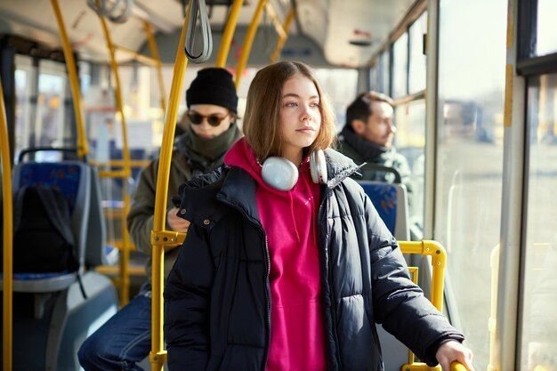 Concentrati su una giovane ragazza con le cuffie in piedi in un tram moderno con persone sfocate sullo sfondo