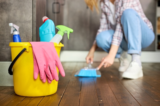 Concentrati sul secchio con guanti di gomma e detergenti all'interno, casalinga che rimuove polvere e sporco dal pavimento usando spazzola e paletta, pulisce la casa.