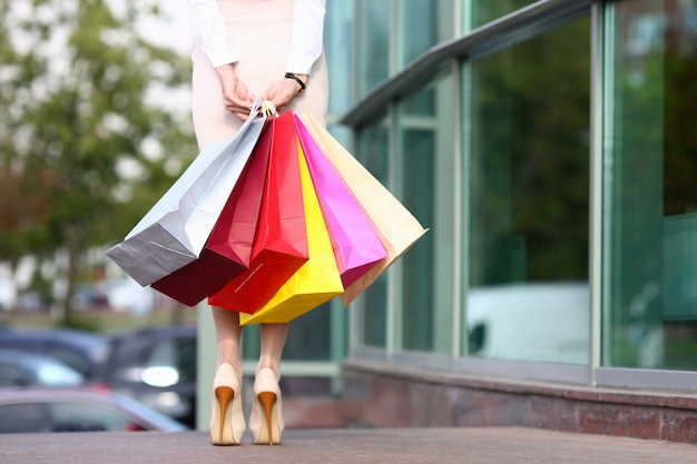 Concentrati sulla bellissima modella in abiti leggeri in piedi vicino a boutique alla moda e in possesso di pacchetti negozio multicolore. Concetto di moda e shopping.