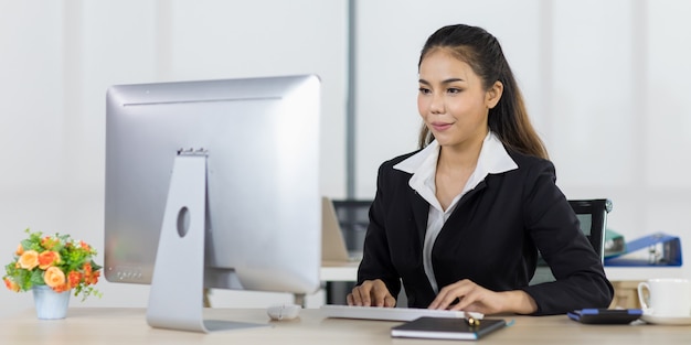 Concentrati sulle persone dell'ufficio delle donne asiatiche che indossano un abito seduto alla scrivania e usano il computer mentre sorridono con gioia.
