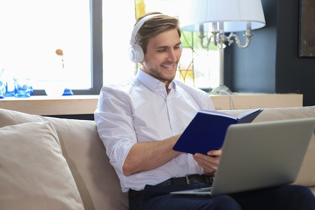 Concentrato giovane uomo d'affari freelance seduto sul divano con il computer portatile e l'esame dei documenti.