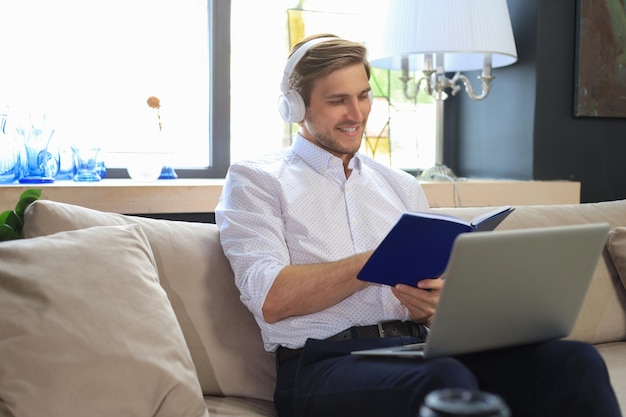 Concentrato giovane uomo d'affari freelance seduto sul divano con il computer portatile ed esaminando i documenti.