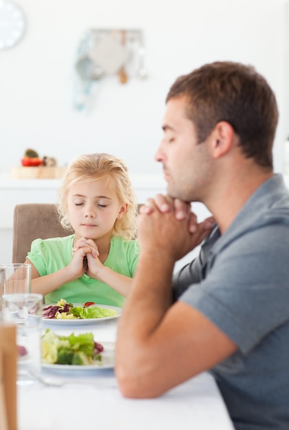 Concentrato padre e figlia pregando prima di mangiare la loro insalata
