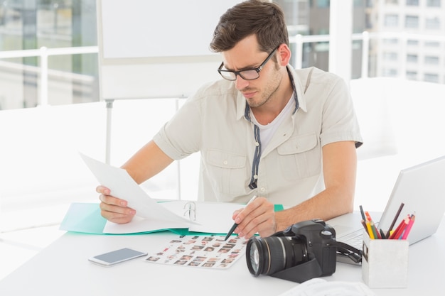 Concentri l&#39;artista maschio che si siede allo scrittorio con le foto