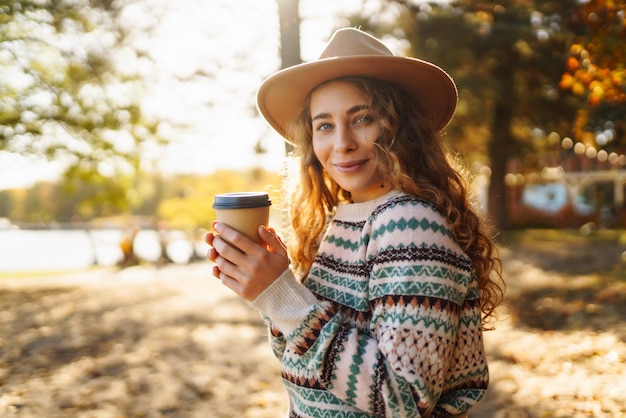 Concept autunnale donna che beve caffè su una panchina sullo sfondo del lago che si gode della solitudine con la natura