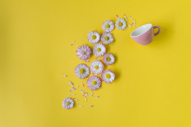 Concept creativo con una tazza rosa e fiori su uno sfondo giallo