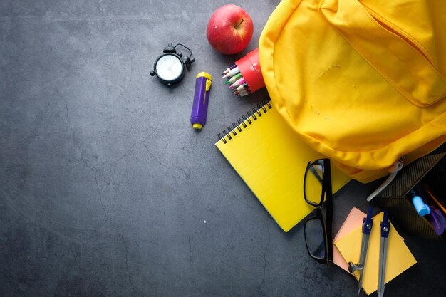 Concept di ritorno a scuola con zaino giallo e rifornimenti scolastici