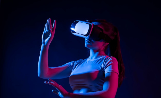 Concept tecnologico del futuro Giovane donna che indossa un auricolare VR e guarda video 360 in luce al neon Donna che tocca oggetti virtuali in occhiali VR persona