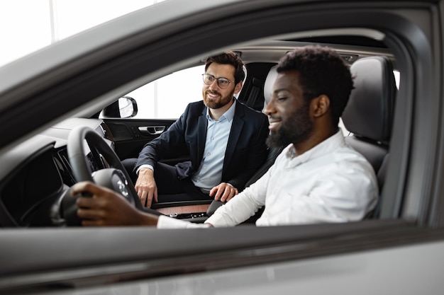 Concessionario di auto caucasico con un acquirente afroamericano all'interno del veicolo
