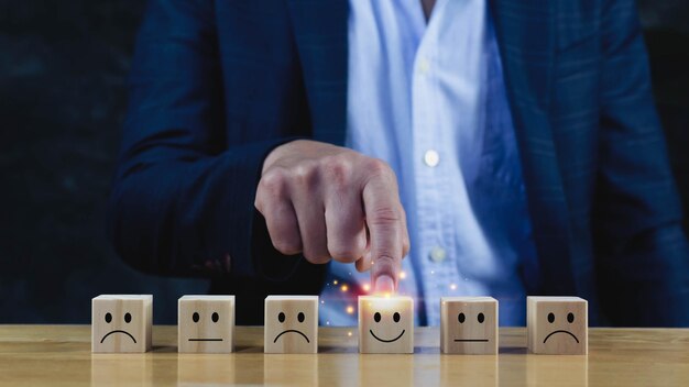 Concetti di valutazione del servizio di valutazione del servizio clienti e sondaggio sulla soddisfazione La mano dell'uomo d'affari sceglie il blocco di legno con l'icona del viso sorridente sul cubo di legno