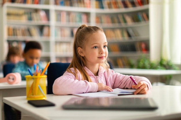 Concetto accademico intelligente scolaressa caucasica seduta alla scrivania in classe ascoltando l'insegnante e