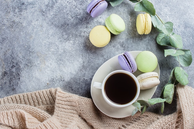 Concetto accogliente mattina. Deliziosi macarons colorati pastello con crema e caffè, caldo maglione grigio