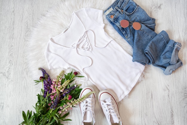 Concetto alla moda. Stile di strada. T-shirt bianca con allacciatura, jeans, scarpe da ginnastica e mazzi di fiori.