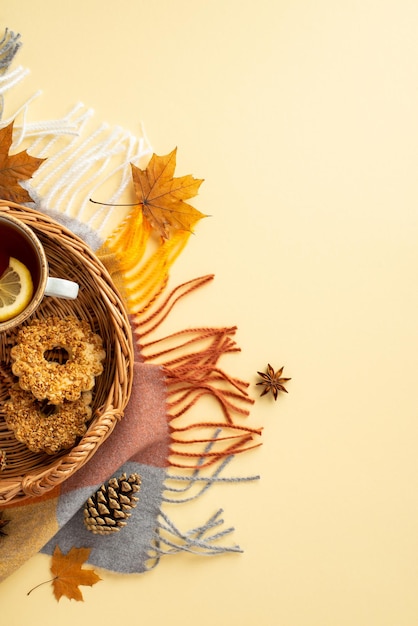 Concetto autunnale Foto verticale superiore di vassoio di vimini con una tazza di tè con biscotti a fette di limone, anice, foglie di acero giallo, cono di pino e quadri su uno sfondo beige pastello isolato