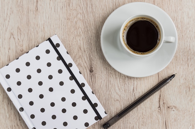 Concetto dell'ufficio e di affari - taccuino, penna e tazza in bianco e nero della copertura del pois di caffè nero sulla tavola di legno. vista dall'alto.