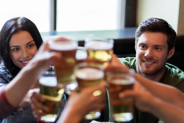 Concetto della gente, di svago, di amicizia e di comunicazione - amici felici che bevono birra, chiacchiere e tintinnio al bar o al pub