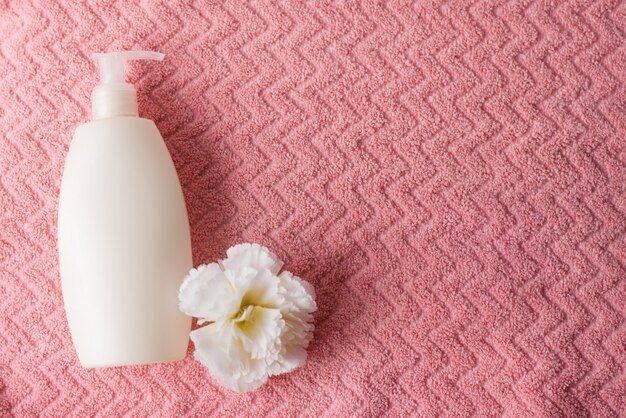 Concetto della stazione termale su fondo rosa, disposizione piana del fiore bianco e della bottiglia dello spruzzo