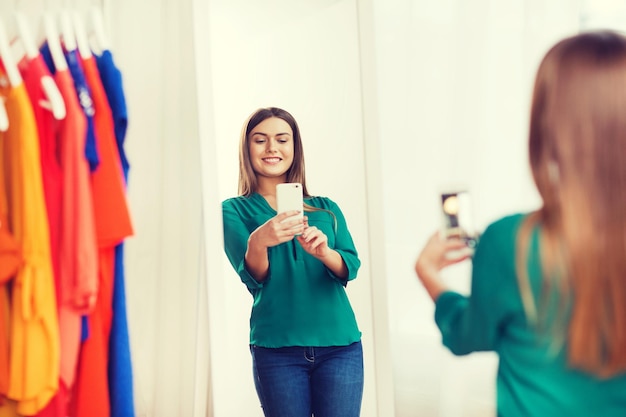 concetto di abbigliamento, moda, stile, tecnologia e persone - donna felice con smartphone che prende selfie allo specchio nel guardaroba di casa