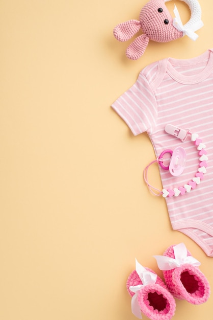 Concetto di accessori per bambini Vista dall'alto foto verticale di vestiti per bambini tuta rosa stivaletti a maglia giocattolo sonaglio coniglietto e catena ciuccio su sfondo beige pastello isolato