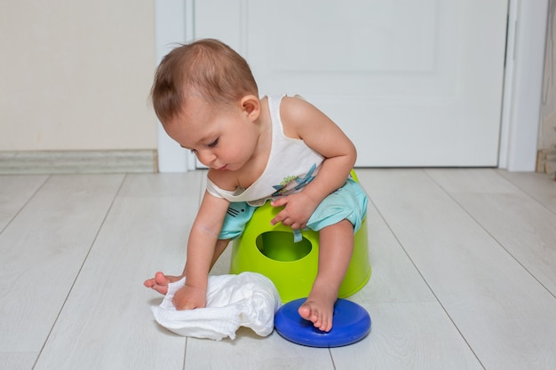 Concetto di addestramento al vasino Un bambino carino si siede su un vaso verde e gioca con un pannolino nella stanza