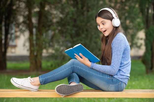 Concetto di adolescente Adolescente ragazza felice che legge e ascolta l'audiolibro in cuffia