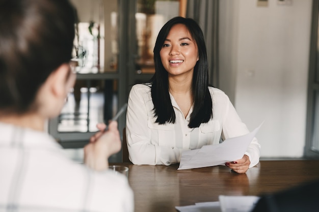 Concetto di affari, carriera e posizionamento - donna asiatica gioiosa che sorride e che tiene il curriculum, mentre era seduto davanti ai direttori durante la riunione aziendale o il colloquio di lavoro