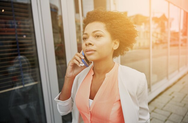concetto di affari, comunicazione, tecnologia e persone - giovane donna d'affari afroamericana che chiama smartphone in città