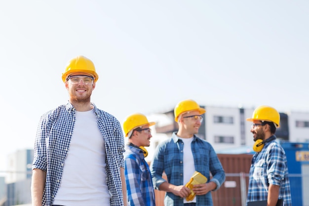 concetto di affari, costruzione, lavoro di squadra e persone - gruppo di costruttori sorridenti in elmetti protettivi all'aperto