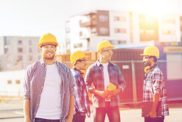 concetto di affari, costruzione, lavoro di squadra e persone - gruppo di costruttori sorridenti in elmetti protettivi con appunti all'aperto