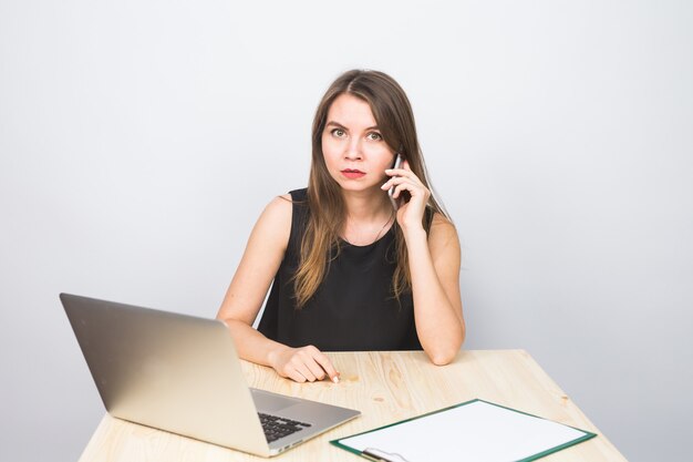 Concetto di affari - donna di affari che parla sul telefono in ufficio e che lavora al computer portatile.